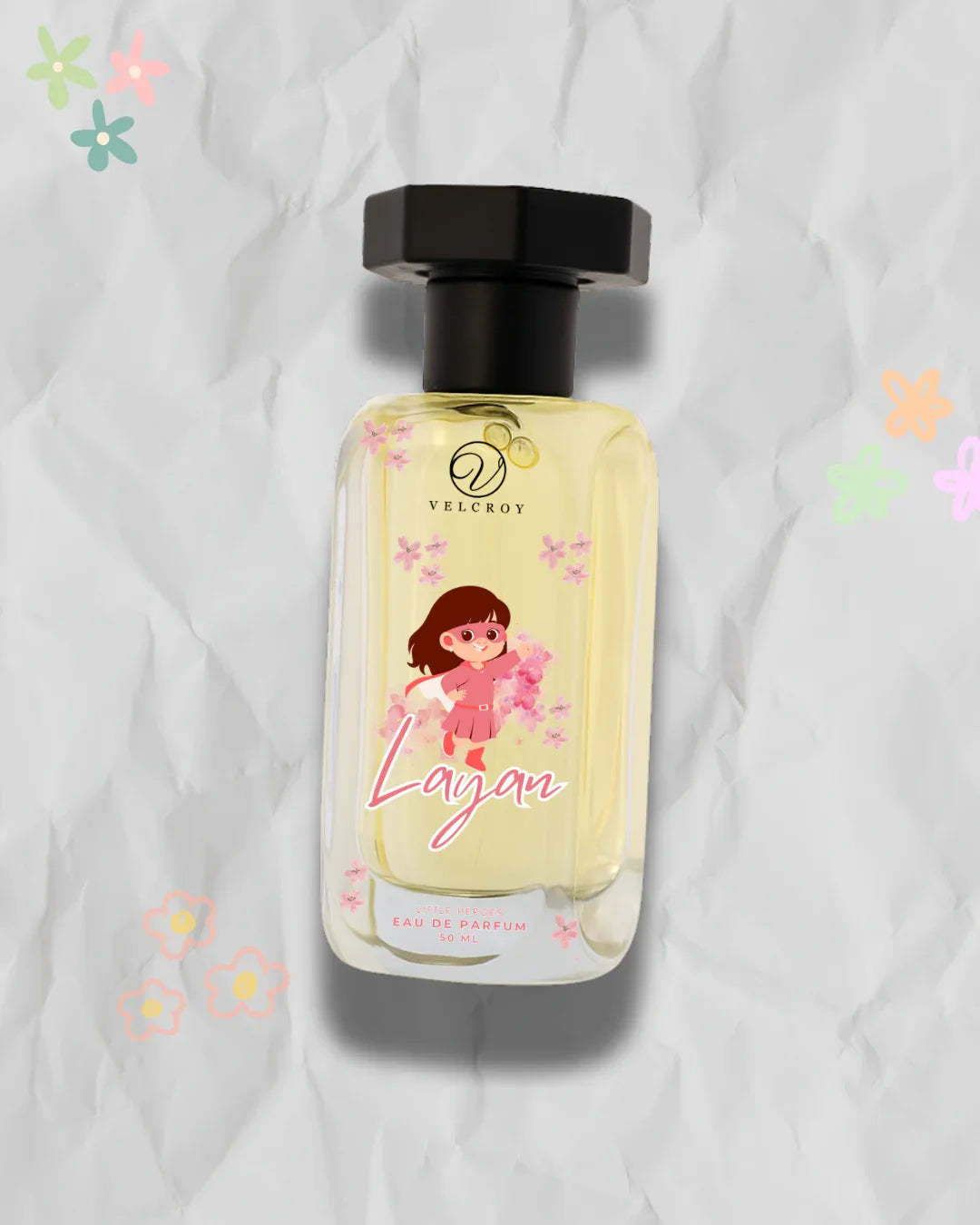 Perfume bottle labeled 'Layan' with cartoon girl, floral accents, and black cap on textured background