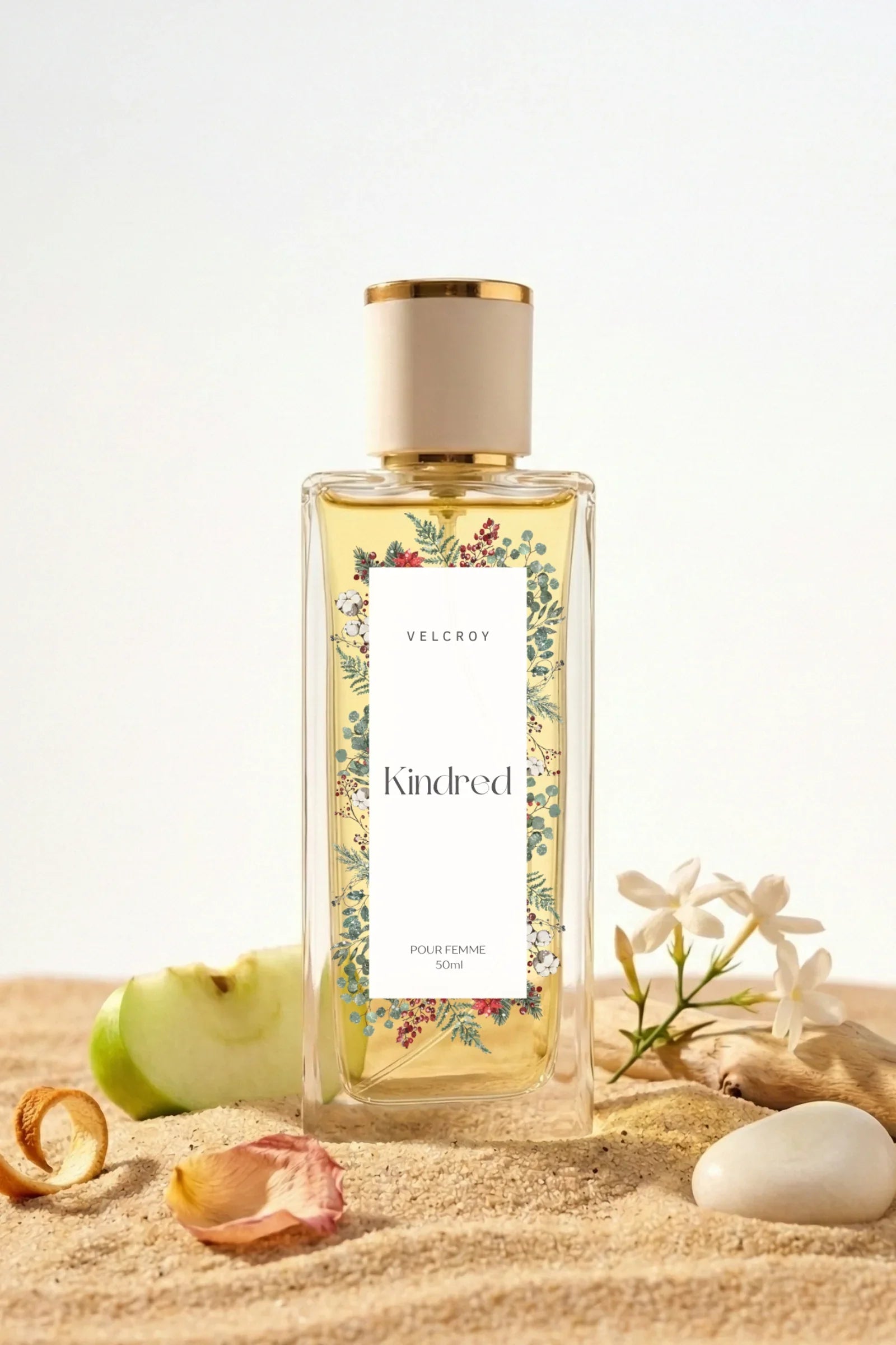Luxury floral perfume bottle on sand with apple slice, white flowers, and decorative label