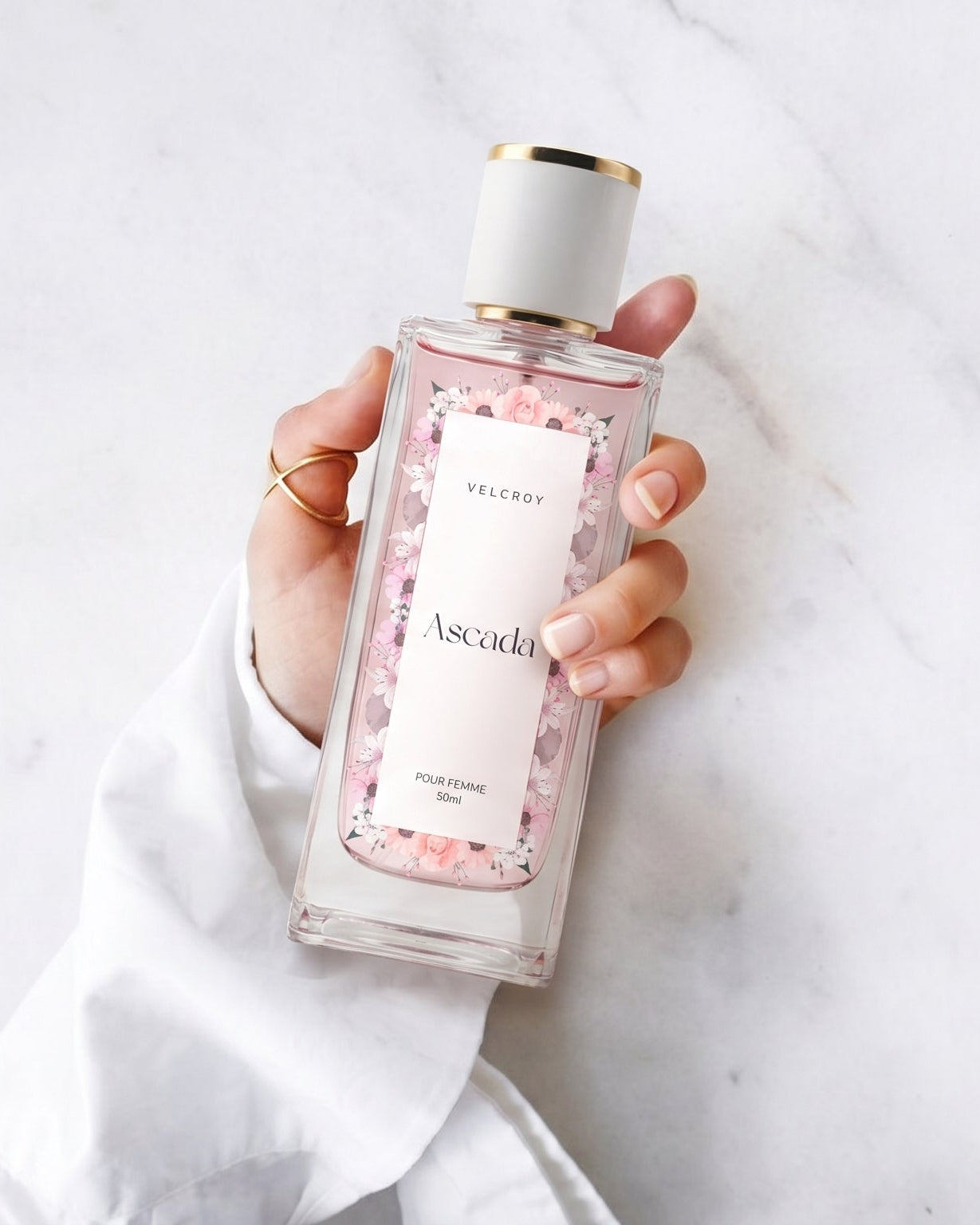 A hand holding a clear rectangular bottle of Ascadi Rose Petal Shower Gel against a white marble background.