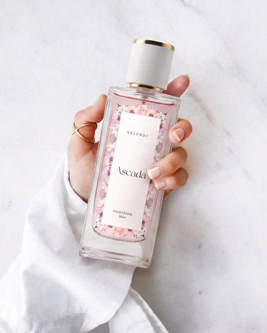A hand holding a clear rectangular bottle of Ascadi Rose Petal Shower Gel against a white marble background.