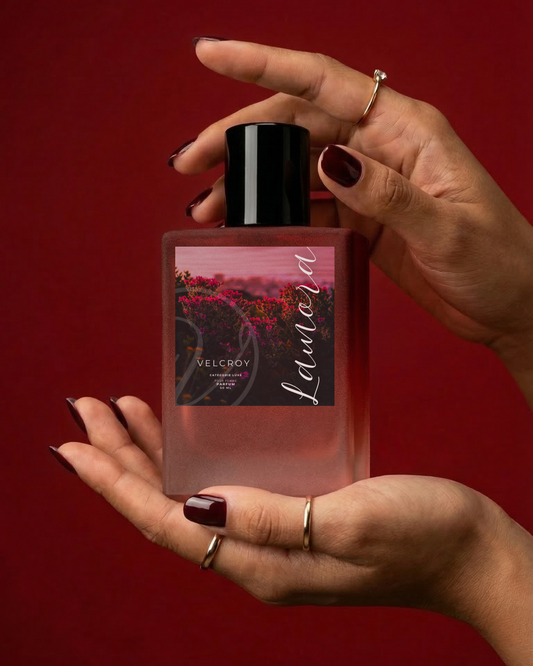 Hand holding a perfume bottle with a red background.
