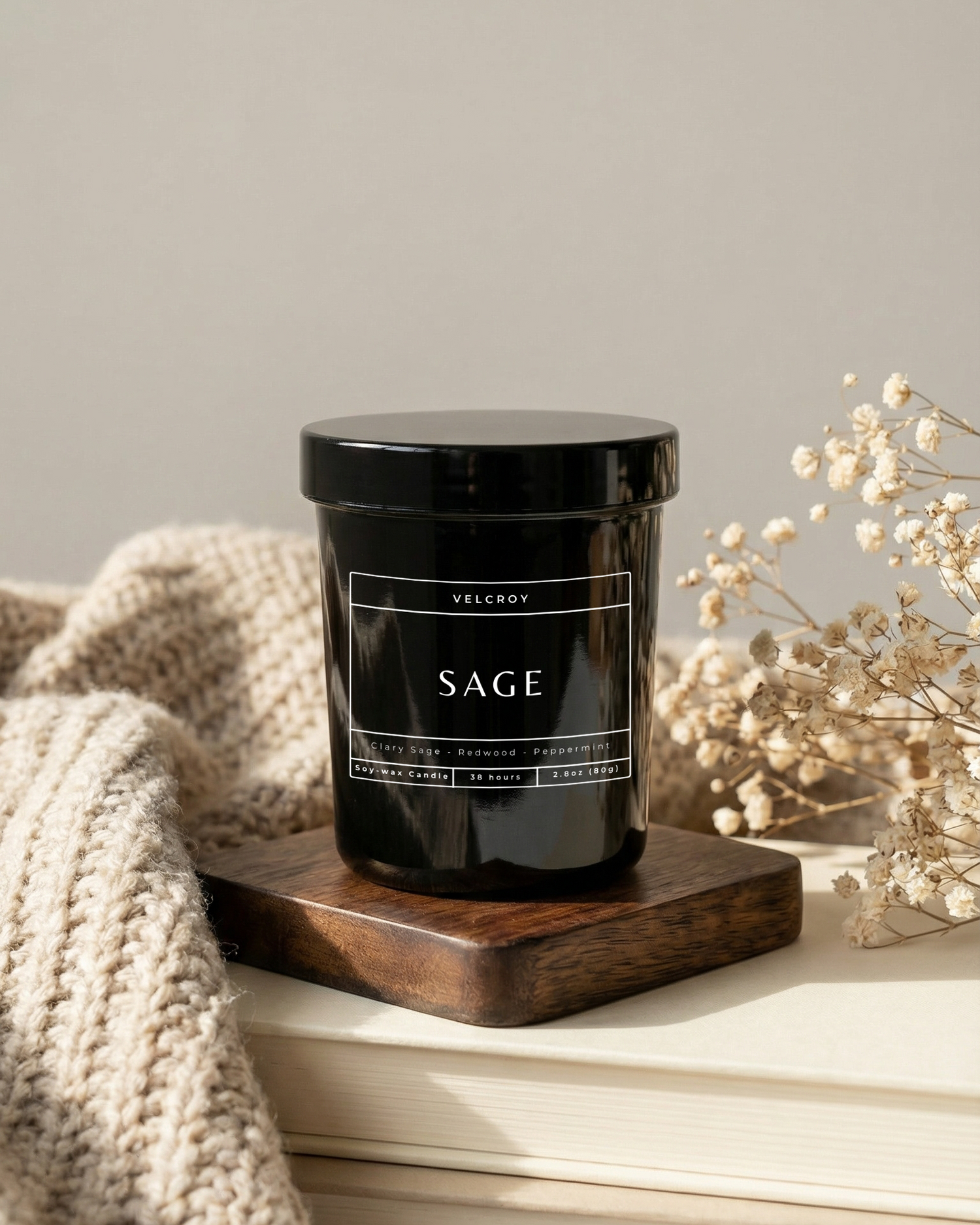Black candle labeled 'SAGE' on a wooden coaster with a neutral background