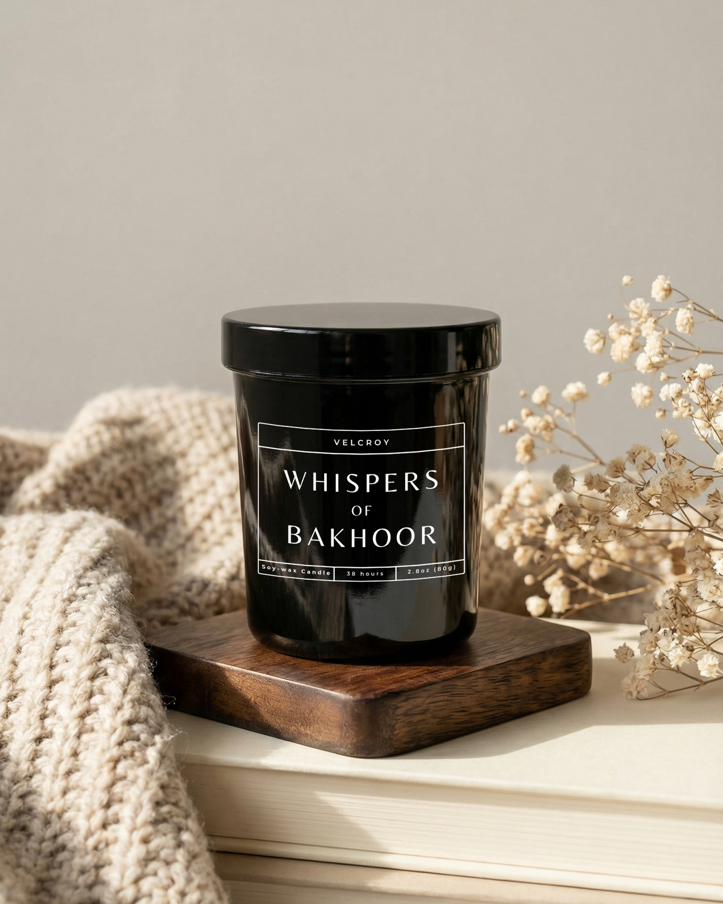 Candle labeled 'Whispers of Bakhoor' on a wooden coaster with a neutral background